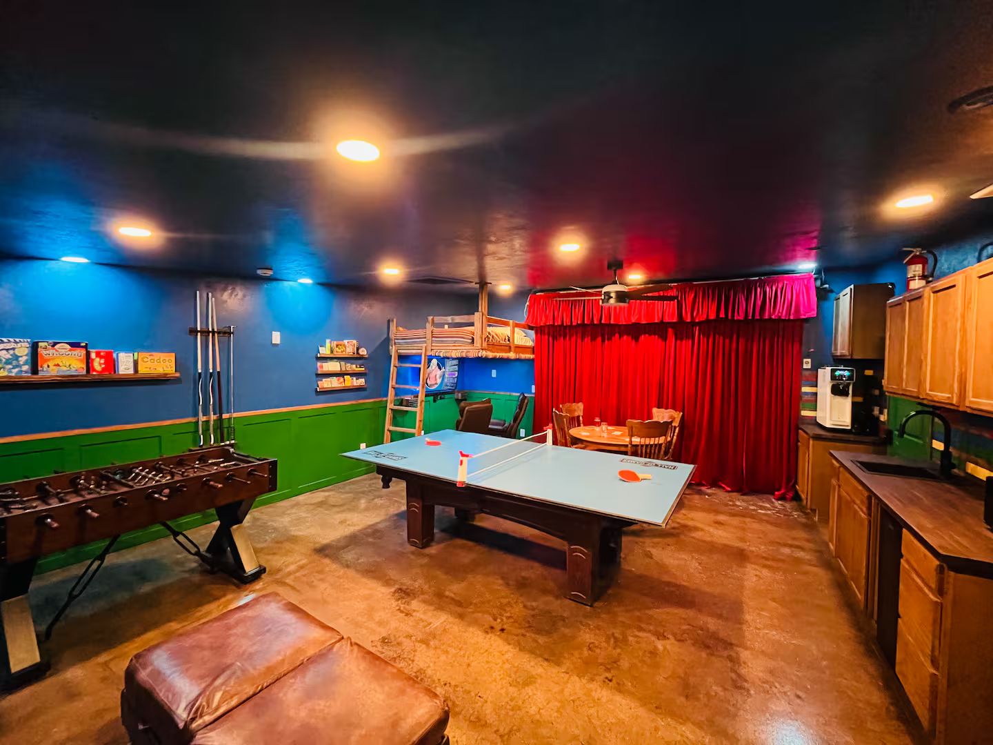 Una habitación con mesa de fútbol de mesa, mesa de ping pong y mesa de fútbol de mesa con un telón rojo de fondo.