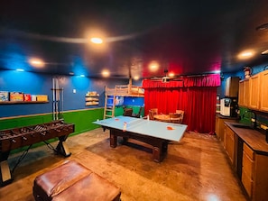 A room with a foosball table, ping pong table, and a foosball table with a red curtain backdrop. - 12 BDR ID Retreat, Hot Tub, beds for 37+, Events (Nampa)