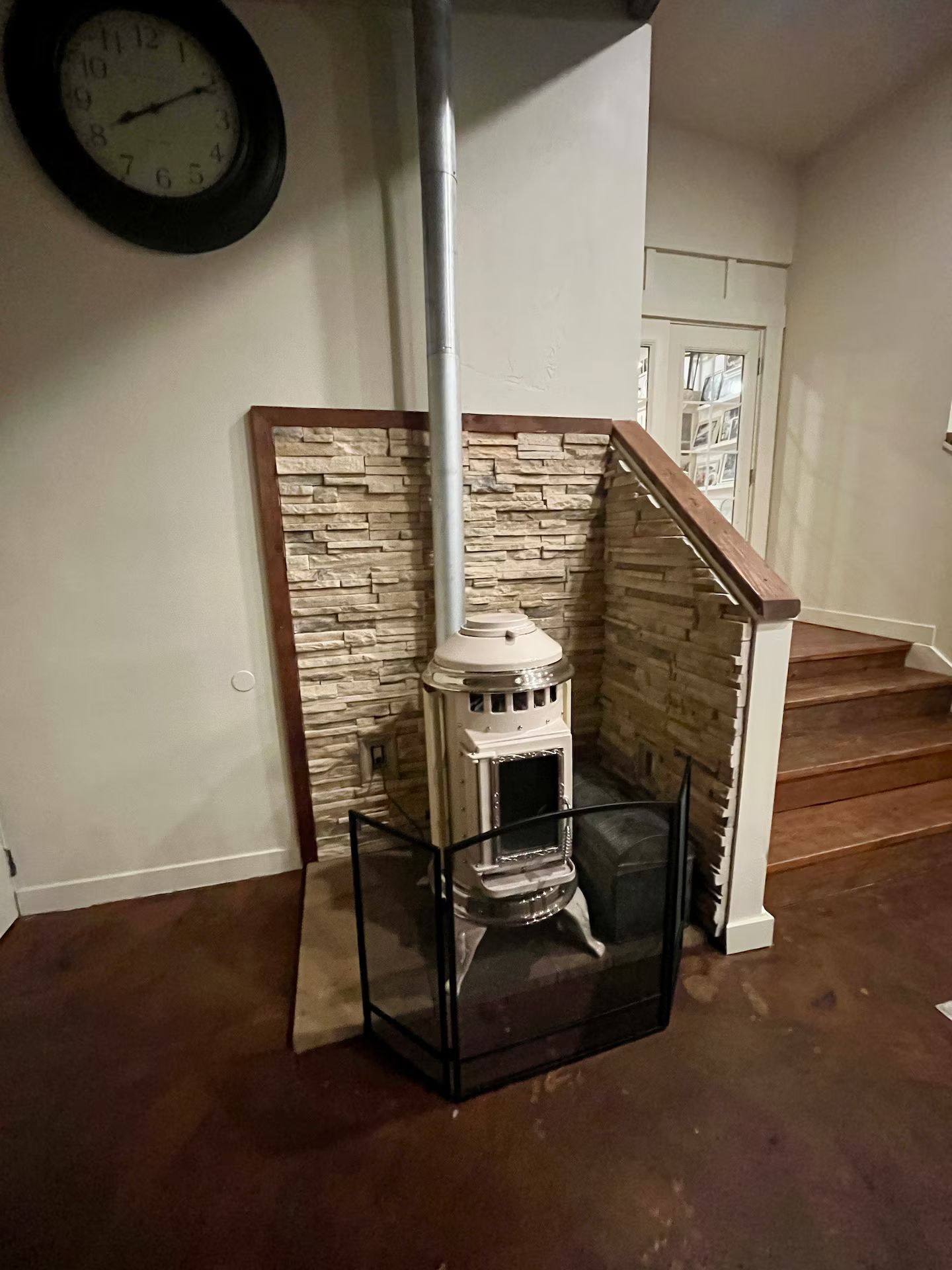 Ein Kamin aus Stein mit einer Glasschiebetür, eine Wanduhr und eine Treppe im Hintergrund.