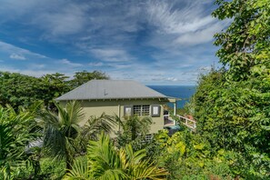 A house with a sloped roof, surrounded by lush greenery and overlooking a body of water. - 5BR Villa w/pool in peaceful residential neighborhood (Charlotte Amalie West)