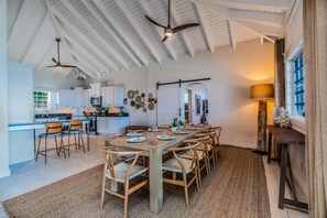 Une cuisine spacieuse avec des meubles blancs, un coin repas avec des chaises en bois et un ventilateur de plafond.