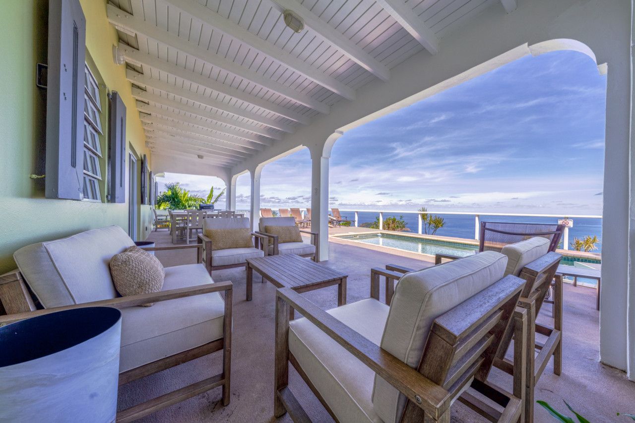 A covered outdoor seating area with a pool and ocean view.