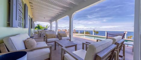 A covered outdoor seating area with a pool and ocean view.