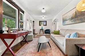 Ein geräumiges Wohnzimmer mit einem roten Schreibtisch, einem grauen Sofa und einem gemusterten Teppich.