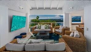 A spacious outdoor living area with wicker furniture, a flat-screen TV, and a view of a mountainous landscape. - Sunset Sanctuary: Gorgeous 5br w/huge pool/deck & lots of space! (St. Thomas)