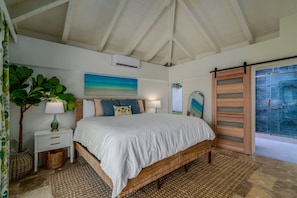 A bedroom with a large bed, a nightstand, a lamp, a potted plant, and a view of the ocean through a sliding door. - Sunset Sanctuary: Gorgeous 5br w/huge pool/deck & lots of space! (St. Thomas)