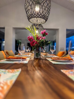 A dining table set for six with a centerpiece of pink flowers, a hanging light fixture above, and a view of the outdoors. - Sunset Sanctuary: Gorgeous 5br w/huge pool/deck & lots of space! (St. Thomas)