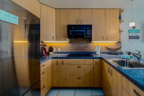 A compact kitchen with wooden cabinets, a black microwave, and a blue countertop. - 1Br condo in Sapphire Beach Resort - pool & beach! Sleeps 4 (St. Thomas)