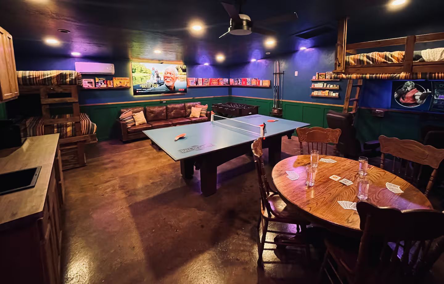 A room with a ping pong table, a sofa, and a table with playing cards.