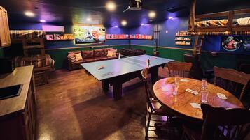 A room with a ping pong table, a sofa, and a table with playing cards.