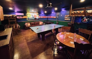A room with a ping pong table, a sofa, and a table with playing cards.