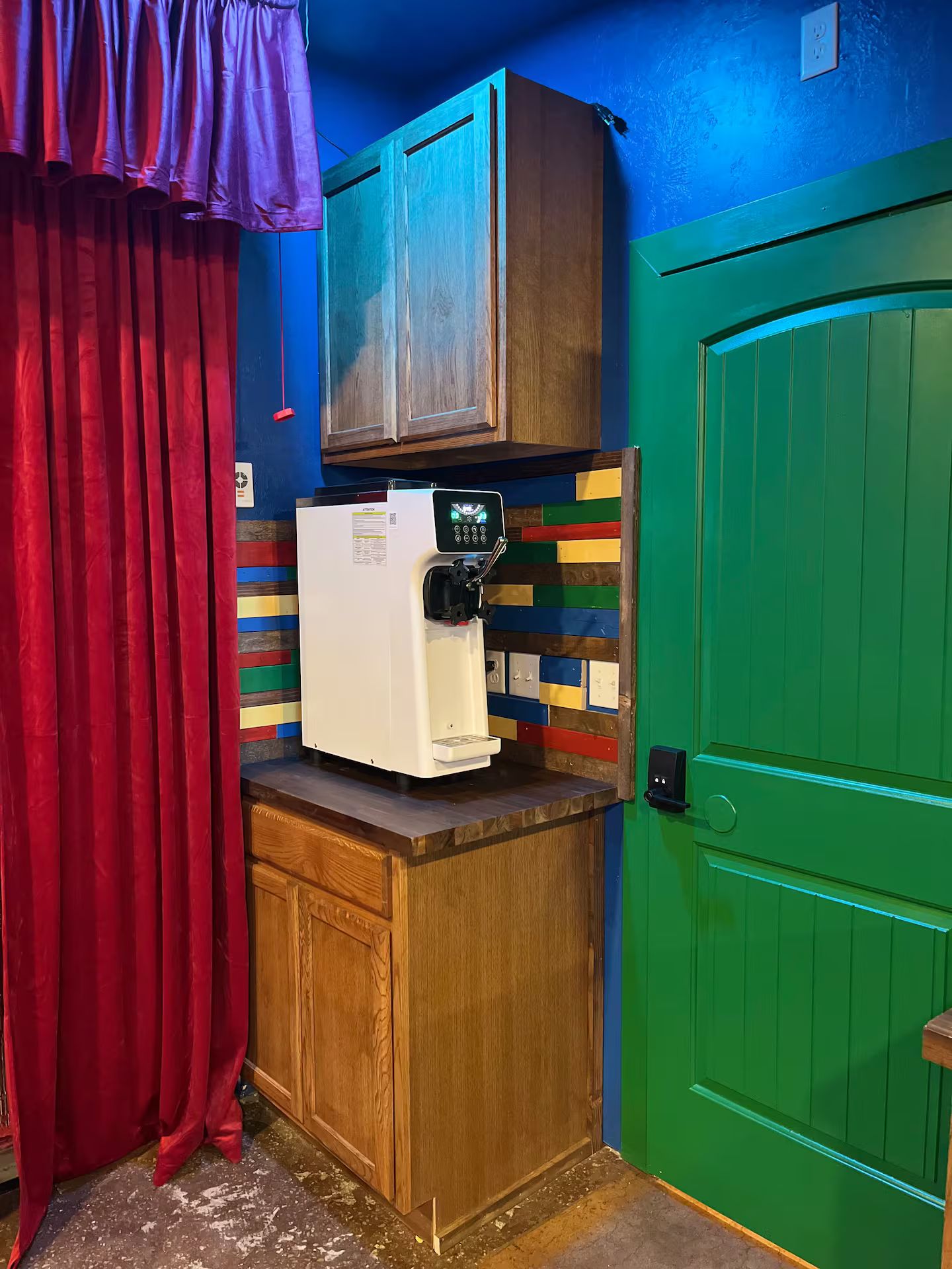A compact kitchenette with a coffee machine, wooden cabinets, and a green door.