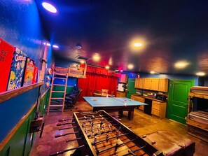 A room with a foosball table, a bunk bed, and a kitchenette area.