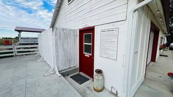 A white building with a red door, a sign with general guidelines, and a metal container on the ground.