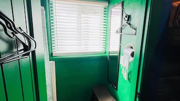 Un baño pequeño con paredes verdes, una ventana, un espejo y un banco.
