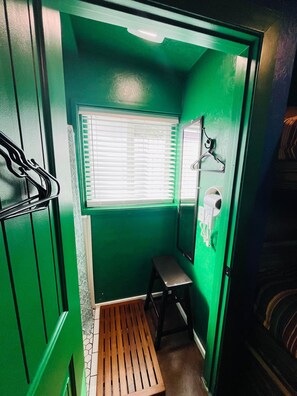 A small, green-walled bathroom with a window, a mirror, and a bench.