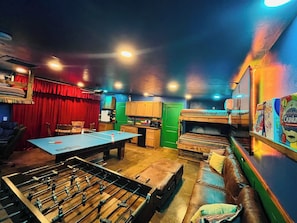 A room with a foosball table, a sofa, a green door, and a red curtain.