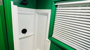 Un área de ducha pequeña y cerrada, con paredes de azulejos blancos y un patrón de suelo hexagonal.