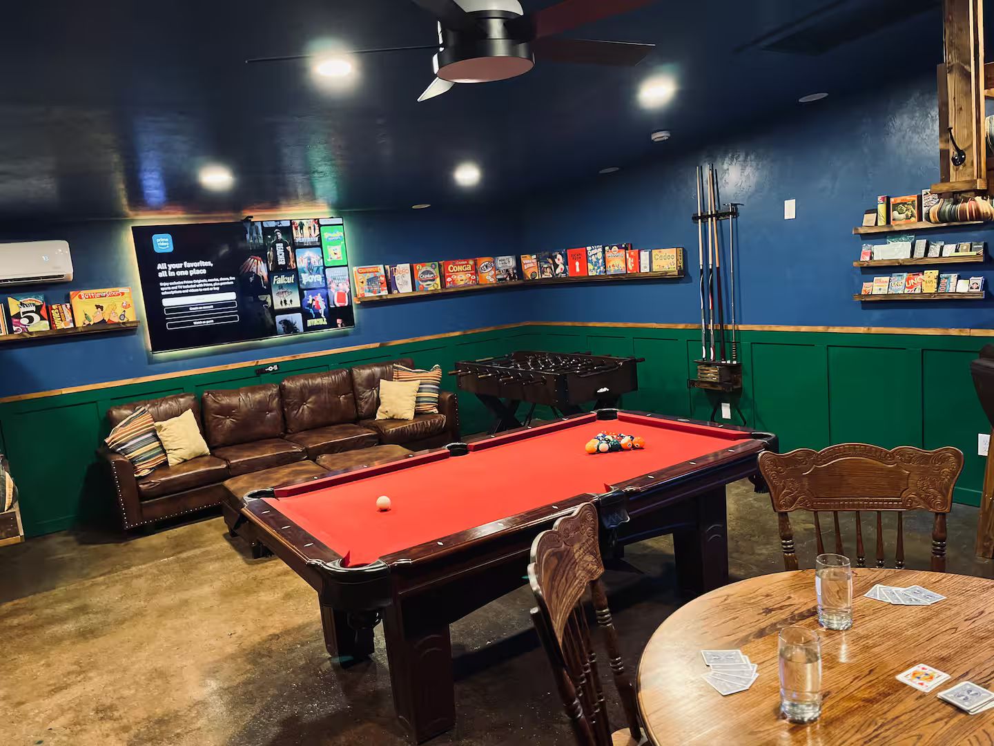 Una sala de billar con mesa de pool, un sofá y una mesa con cartas.