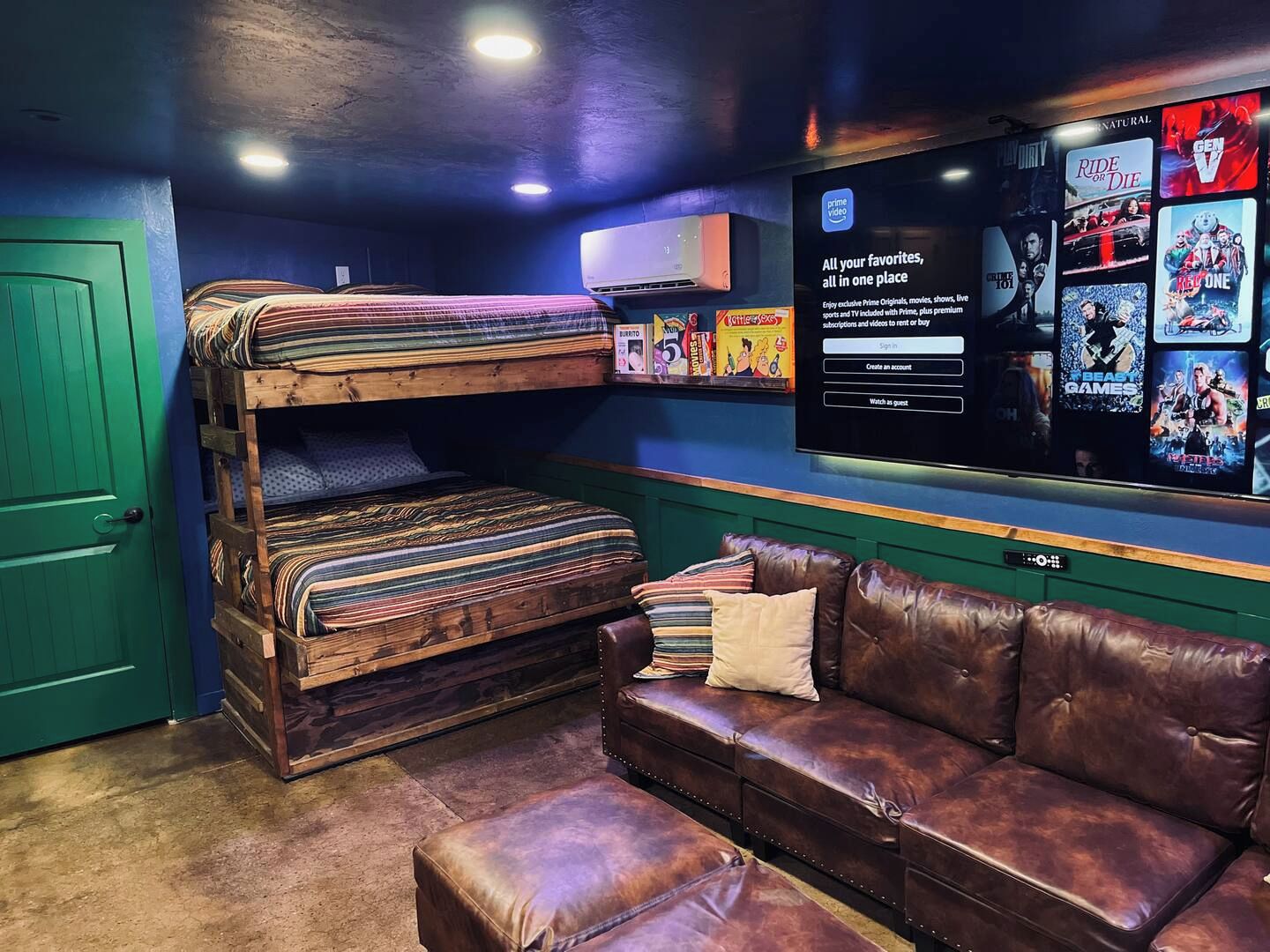 Een kamer met een stapelbed, een leren bank en een aan de muur bevestigde televisie waarop film posters te zien zijn.