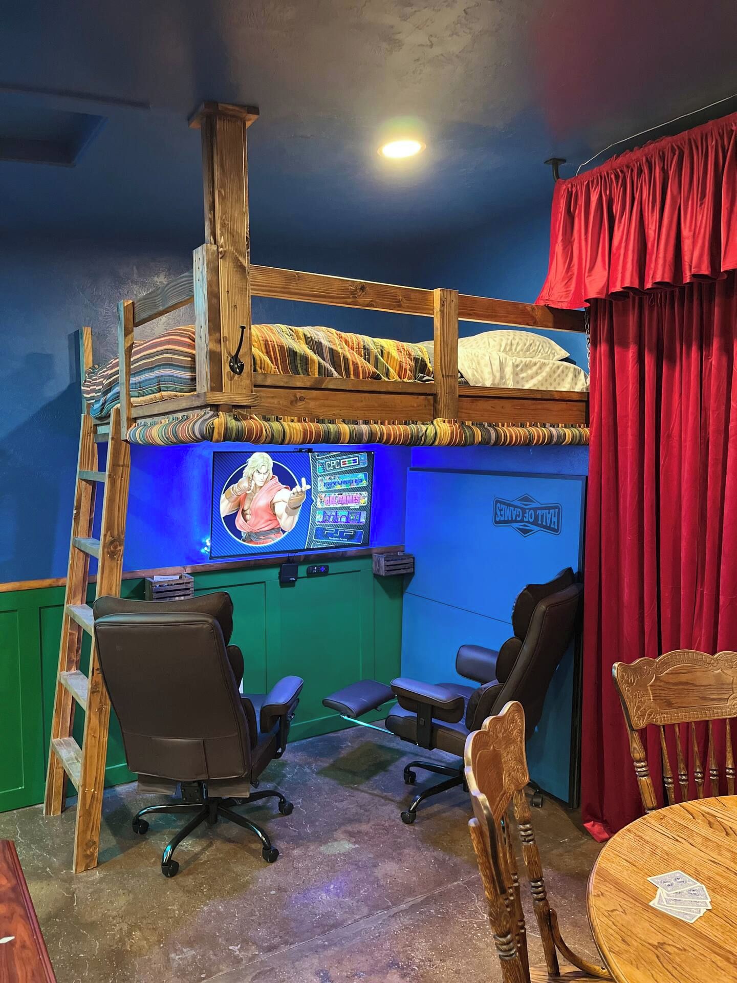 A room with a bunk bed, gaming chairs, a desk with a computer, and a red curtain.