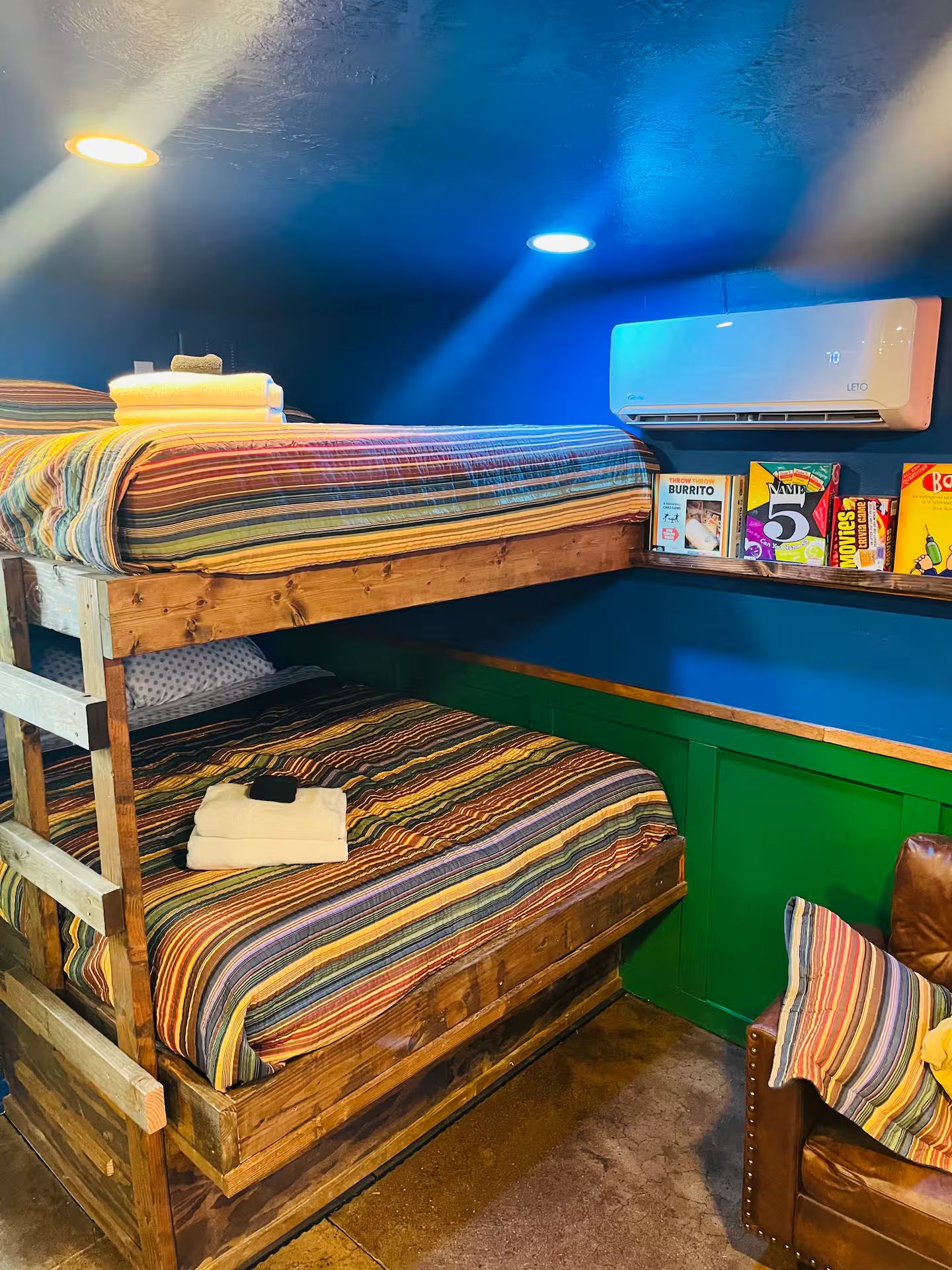 Une chambre avec un lit superposé, un mur vert, un climatiseur fixé au mur et une étagère contenant des collations et un lecteur DVD.