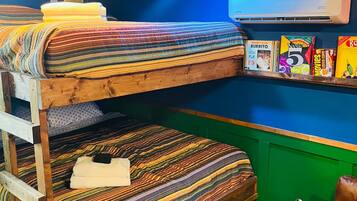 Une chambre avec un lit superposé, un mur vert, un climatiseur fixé au mur et une étagère contenant des collations et un lecteur DVD.