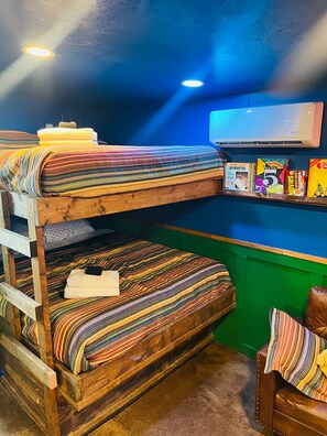 A bunk bed room with a green wall, a mounted air conditioner, and a shelf with snacks and a DVD player.