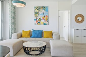 A modern living room with a sofa, a round coffee table, and a painting of colorful surfboards. - Marina Retreat by IIM (Estepona)