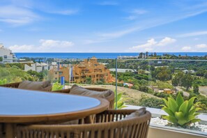 A terrace with a table and chairs overlooking a coastal view with buildings and greenery. - Marina Retreat by IIM (Estepona)