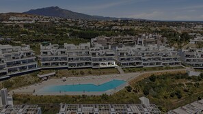 A modern residential complex with multiple buildings, a swimming pool, and a view of the surrounding landscape. - Marina Retreat by IIM (Estepona)