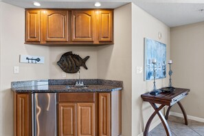 A kitchen with wooden cabinets, a granite countertop, a stainless steel dishwasher, a fish-shaped wall decoration, and a painting on the wall. - Colonnades 302 (Gulf Shores)
