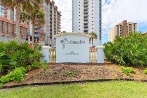 A sign for The Colonades at 527 East Beach Boulevard, surrounded by greenery and tall buildings. - Colonnades 302 (Gulf Shores)