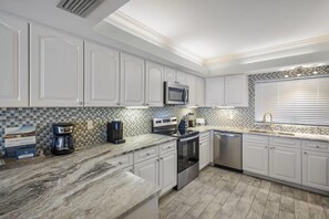 A modern kitchen with white cabinetry, a built-in microwave, stainless steel appliances, and a tiled backsplash. - Shipwatch D302 (Pensacola)
