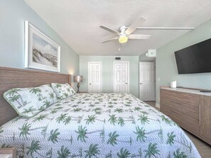 A bedroom with a bed, a ceiling fan, a TV, and two doors. - Island House Beach Club 5D - Beautiful Beachfront Condo (Fort Myers Beach)