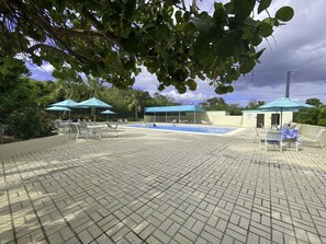 Un área de piscina al aire libre con suelo de baldosas, sillas de descanso y sombrillas.
