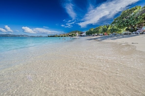 A beach with clear shallow waters, a sandy shore, and a few people swimming. - 1BR condo on Sapphire Beach - sleeps 4! (St. Thomas)