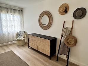 A room with a wicker chair, a black and wicker console, a mirror, and three hats on a wall. - 1BR condo on Sapphire Beach - sleeps 4! (St. Thomas)