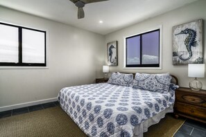 A bedroom with a bed, two windows, a ceiling fan, and artwork on the walls. - Magen`s Bay Villa | Tesla Solar Power (St. Thomas)