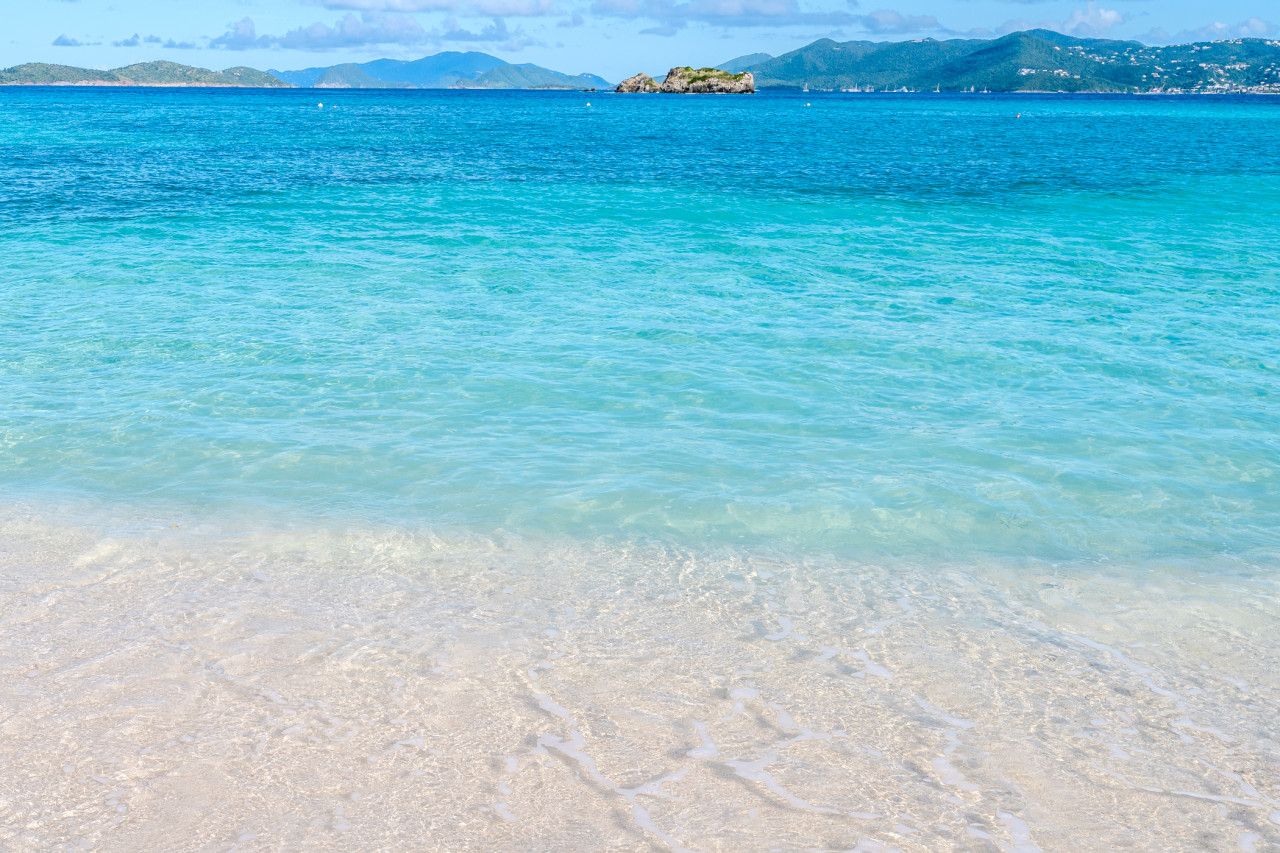 A beach with clear turquoise water and a distant rocky island.