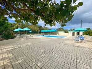A pool area with tiled flooring, lounge chairs, and umbrellas. - 1BR Condo On the Beach! Sleeps 4 (St. Thomas)