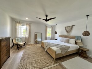 Ein Schlafzimmer mit einem Bett, einem Sessel, einer Kommode, einem Spiegel und einem Deckenventilator.