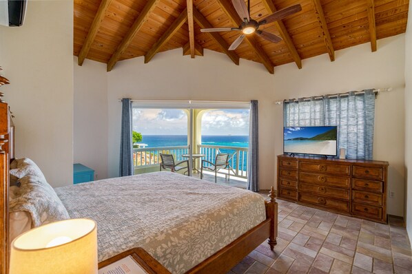 Ein Schlafzimmer mit einem großen Bett, einem Deckenventilator, einem Fernseher und einem Balkon mit Meerblick.