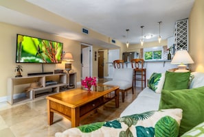 A living room with a wooden coffee table, a sofa, and a television mounted on the wall. - Amazing Location & Value! A few steps to the beach, walk to the restaurant/bar! (St. Thomas)