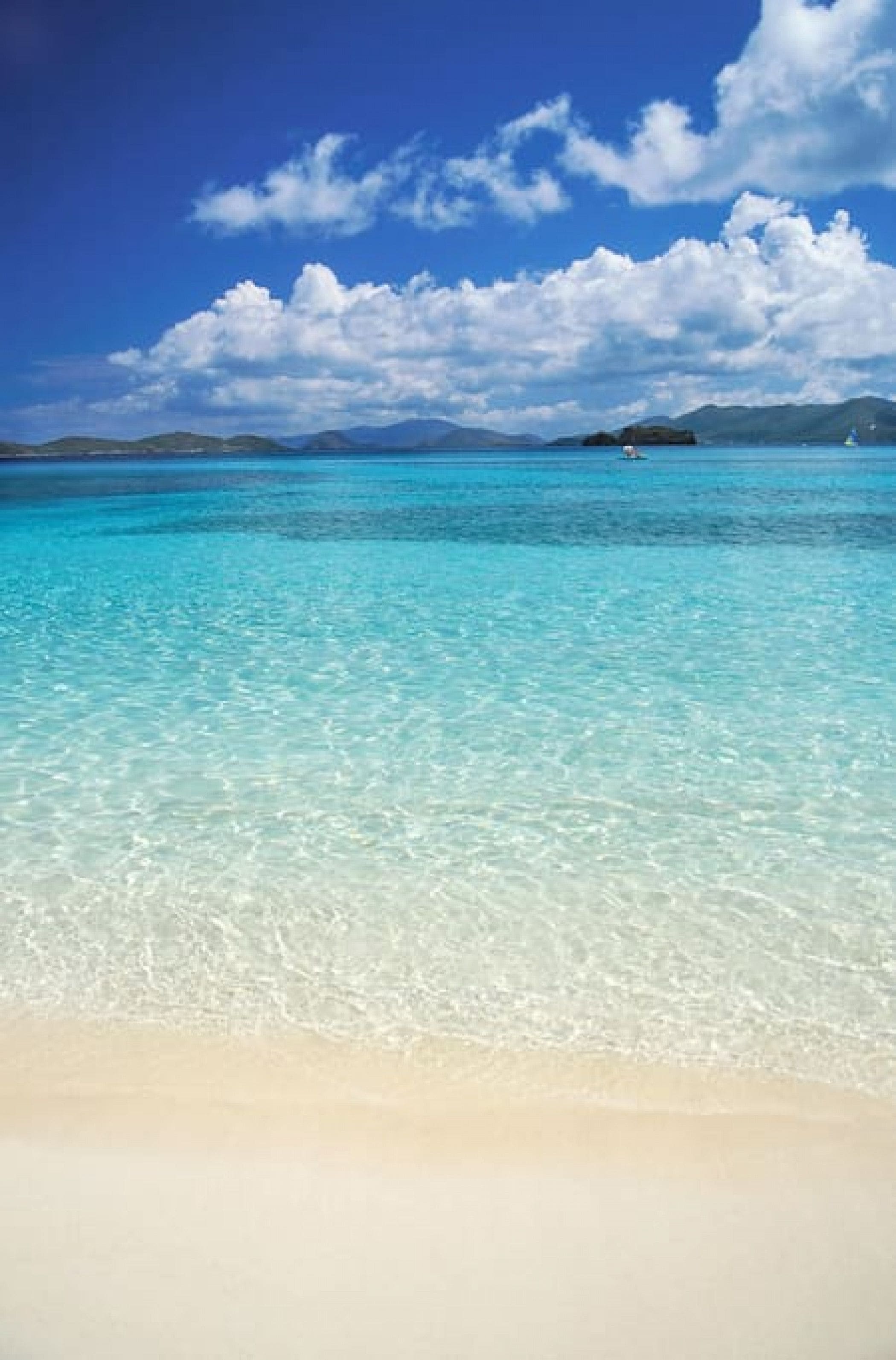 Una playa con agua turquesa cristalina y una orilla arenosa bajo un cielo azul con nubes.