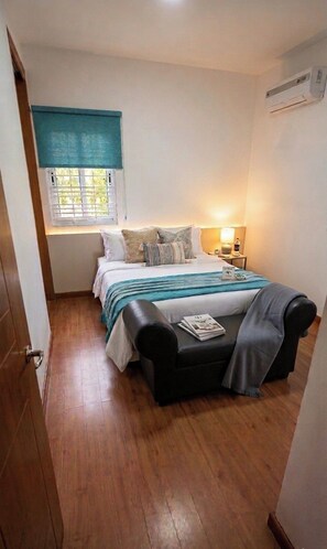 A bedroom with a bed, bedside table, lamp, and a window with blinds. - Porlamar Lomas del Encanto | Relaxation, Comfort & Terrace with a View of the Pool (Porlamar)