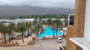 A swimming pool surrounded by palm trees, with a view of distant mountains and buildings. - Porlamar Lomas del Encanto | Relaxation, Comfort & Terrace with a View of the Pool (Porlamar)