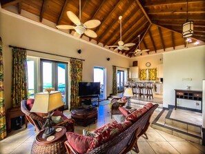 A spacious living area with a television, wicker furniture, and a ceiling fan. - Incredible 3 BR Villa with Fabulous 160º Views of Charlotte Amalie Harbor! (St. Thomas)
