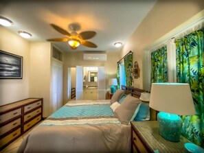 A bedroom with a bed, a ceiling fan, a nightstand, a lamp, and a tropical-themed curtain. - Incredible 3 BR Villa with Fabulous 160º Views of Charlotte Amalie Harbor! (St. Thomas)