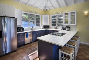 A modern kitchen with a central island, stainless steel appliances, and white cabinetry. - CalypsoBlu - Beautiful views of Morningstar Beach and the cruise ships entering and leaving port!! (St. Thomas)